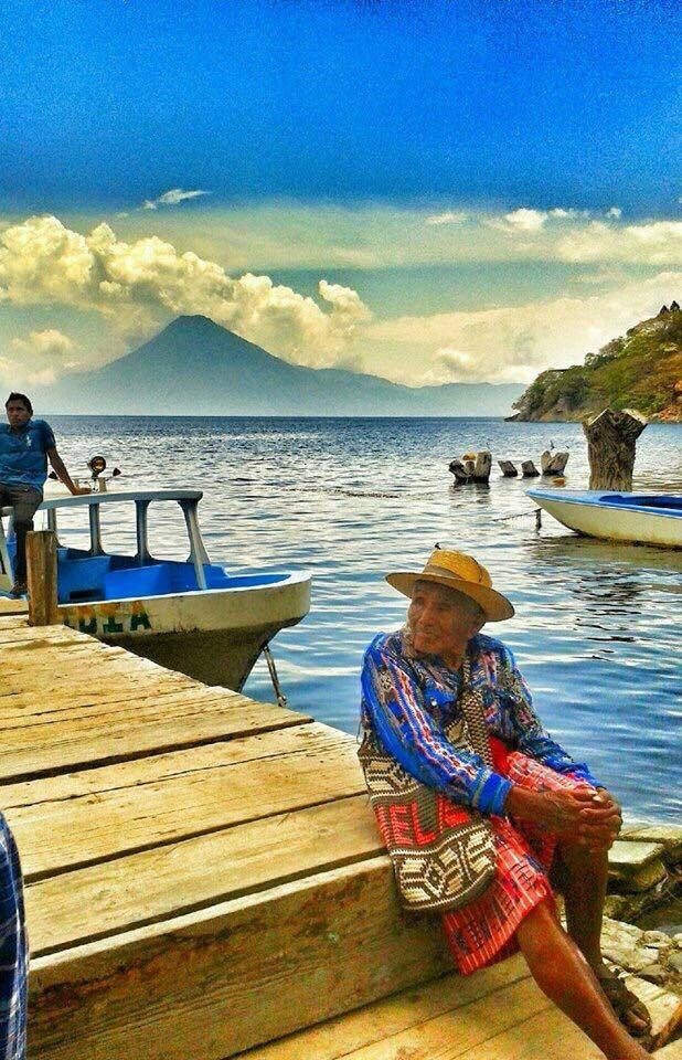 older man dressed in tradional clothes sitting on a boat dock.